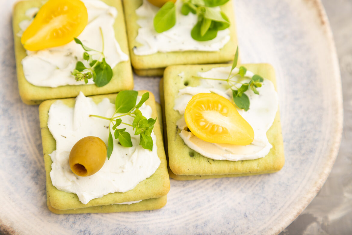Green cracker sandwiches with cream cheese and tomatoes on gray